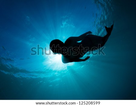 Mermaid silhouette, beautiful young women free diving in the deep blue wearing a mermaid tail monofin
