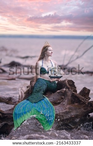 Mermaid story. The little mermaid sits on the seashore. Mermaid at sunset. Mermaid's tail. Mermaid costume. Long hair.