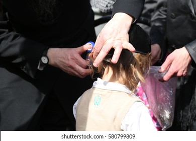 MERON,ISRAEL- MAY 26, 2016: An Unidentified Hasidic Rabbi Gives First Haircut To An Unidentified Jewish Hasidic Boy With Blond Curls As Is Tradition Upon The Grave Of Rabbi Shimon On Lag Ba'omer.

