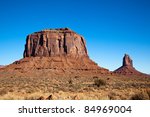 Merrick Butte, a massive eroding orange sandstone formation located on the Navajo Nation in Monument Valley, AZ, is illuminated by morning sun and surrounded by the bright blue January sky.