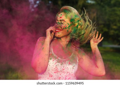 Merry caucasian woman with curly hair standing n a cloud of pink dry paint, celebrating Holi festival - Shutterstock ID 1159639495