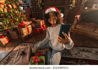 Merry Christmas. African woman in Santa hat having video chat in smartphone. Blogger in festive mood recording video in social network. Girl having video call with friends family celebrating Christmas - Powered by Shutterstock