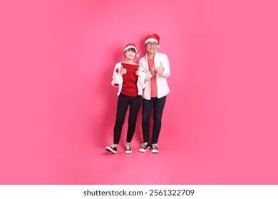 Merry Christmas, Asian senior and young woman wear santa hat and casual red clothes with white heart-shaped shaped shirt jacket with gesture of thumbs up, ok or confirm, isolated on pink background - Powered by Shutterstock