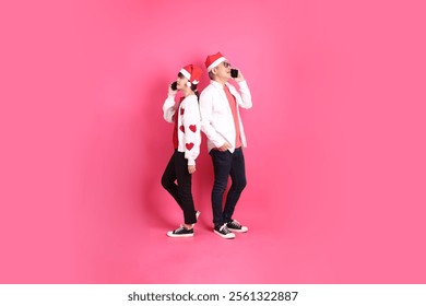 Merry Christmas, Asian senior and young woman wear santa hat and casual red clothes with white heart-shaped shaped shirt jacket with gesture of Holding mobile phone, isolated on the pink background. - Powered by Shutterstock