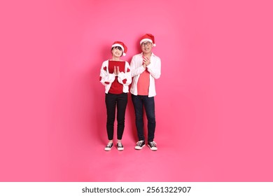 Merry Christmas, Asian senior and young woman wear santa hat and casual red clothes with white heart-shaped shaped shirt jacket with gesture of claping hands isolated on the pink background. - Powered by Shutterstock