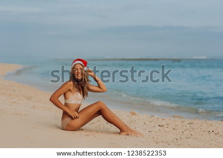 Merry Christmas background concept for holiday season. Happy woman on tropical beach in santa hat sit in sand with ocean
