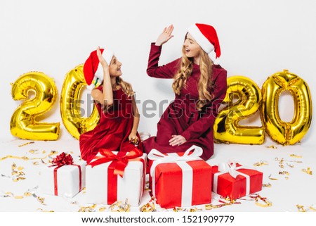 Merry Christmas . Cheerful mom and her cute daughter in Santa hats. A parent and a small child have fun with Christmas gifts on a white background, with balloons in the form of figures 2020