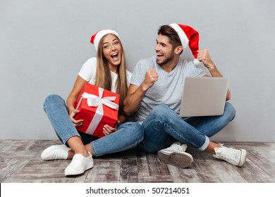 Merry Christmas Couple With Laptop And Gift. Laughing. Gray Background