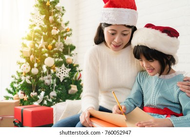 Merry Christmas! Cute Asian Little Child Girl And Her Mother Write The Letter Together To Santa Claus In The Living Room At Home.