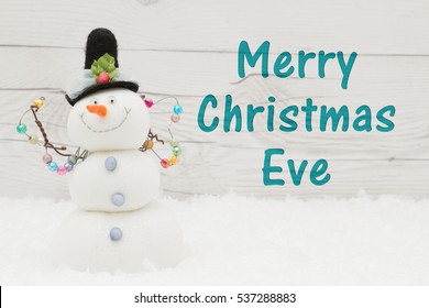 Merry Christmas Eve Greeting, Some Snow And A Snowman On Weathered Wood With Text Merry Christmas Eve