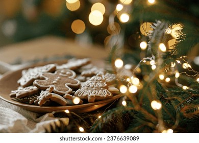 Merry Christmas! Gingerbread cookies with icing in plate on wooden rustic table with fir branches, festive decorations and christmas golden lights. Atmospheric Christmas holidays, family time - Powered by Shutterstock