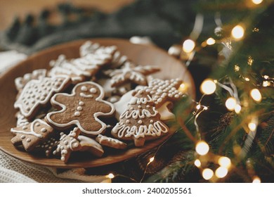 Merry Christmas! Gingerbread cookies with icing in plate on wooden rustic table with fir branches, festive decorations and christmas golden lights. Atmospheric Christmas holidays, family time - Powered by Shutterstock