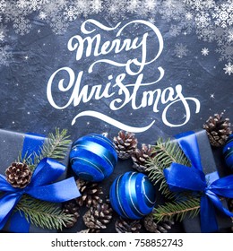 Merry Christmas hand lettering. Christmas gift with blue ribbon and blue balls, tree branches and cones on dark blue background. - Shutterstock ID 758852743