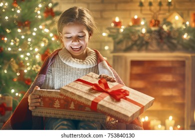 Merry Christmas And Happy Holiday! Cute Little Child Girl With Present Gift Box Near Tree At Home.