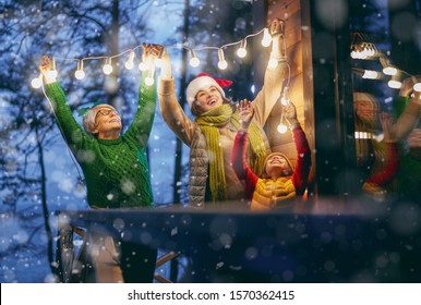 Merry Christmas and Happy Holidays! Cheerful mom, granny and cute girl decorating home. Parents and little child having fun outdoors. Loving family with garlands outside.