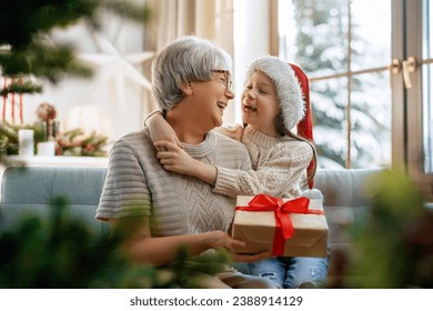 Merry Christmas and Happy Holidays! Cheerful grandma and her cute grand daughter girl exchanging gifts. Granny and little child having fun near tree indoors. - Powered by Shutterstock