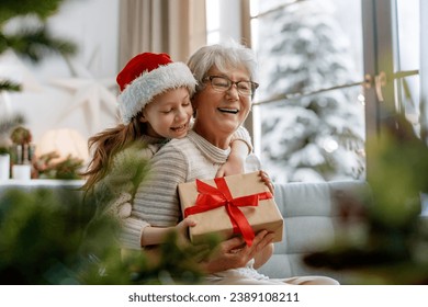 Merry Christmas and Happy Holidays! Cheerful grandma and her cute grand daughter girl exchanging gifts. Granny and little child having fun near tree indoors. - Powered by Shutterstock