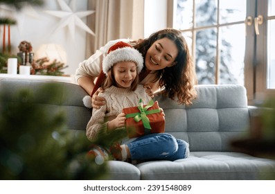 Merry Christmas and Happy Holidays. Cheerful mom and her cute daughter girl exchanging gifts. Parent and little child having fun near tree indoors. - Powered by Shutterstock