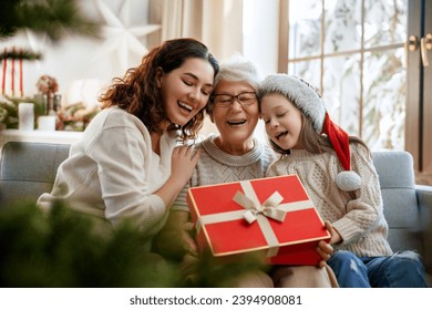 Merry Christmas and Happy Holidays. Cheerful kid presenting gifts to mom and granny. Parents and little child having fun near tree indoors. Loving family with presents in room. - Powered by Shutterstock