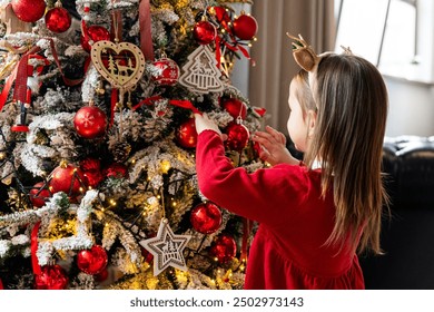 Merry Christmas and Happy Holidays. Cute little child girl is decorating the Christmas tree indoors. - Powered by Shutterstock