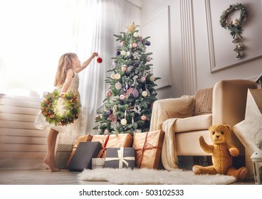 Merry Christmas and Happy Holidays!  Cute little child girl is decorating the Christmas tree indoors.