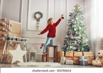 Merry Christmas and Happy Holidays!  Cute little child girl is decorating the Christmas tree indoors.