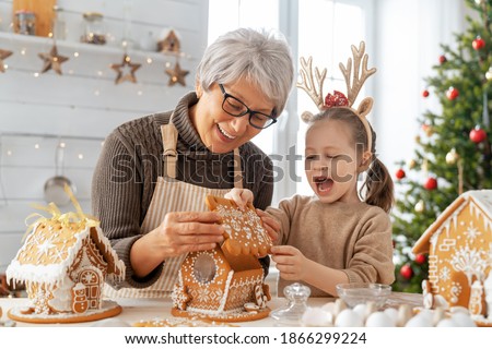 Merry Christmas and Happy Holidays. Family preparation holiday food. Grandmother and granddaughter cooking gingerbread house.
