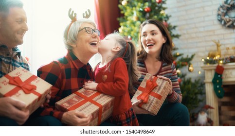 Merry Christmas and Happy Holidays! Grandma, grandpa, mum and child exchanging gifts. Parents and daughters having fun near tree indoors. Loving family with presents in room.                          
