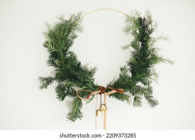 Merry Christmas and Happy Holidays! Modern Christmas wreath with velvet ribbon and golden bells hanging on white wall background. Winter holiday decor, moody image. Boho wreath - Powered by Shutterstock