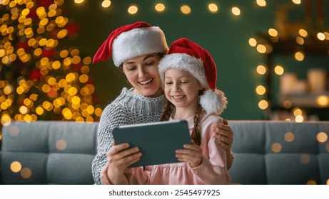 Merry Christmas and Happy Holidays. Mother and child using tablet pc. Parents and daughters having fun near tree indoors. Loving family in the room. - Powered by Shutterstock