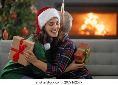 Merry Christmas And Happy Holidays. Senior Mom And Her Adult Daughter Exchanging Gifts. Having Fun Near Tree Indoors. Loving Family With Presents In Room. 