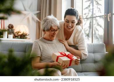 Merry Christmas and Happy Holidays! Senior mom and her adult daughter exchanging gifts. Having fun near tree indoors.  - Powered by Shutterstock