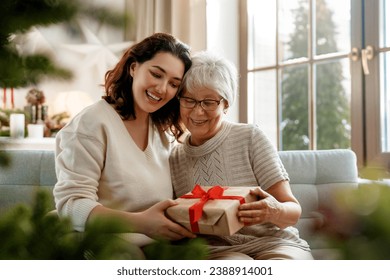 Merry Christmas and Happy Holidays! Senior mom and her adult daughter exchanging gifts. Having fun near tree indoors.  - Powered by Shutterstock