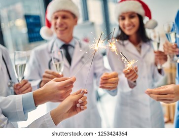 Merry Christmas and Happy New Year! Group of doctors celebrating winter holidays at work. Medical personnel in uniform and Santa Claus hats drinking champagne together. - Powered by Shutterstock