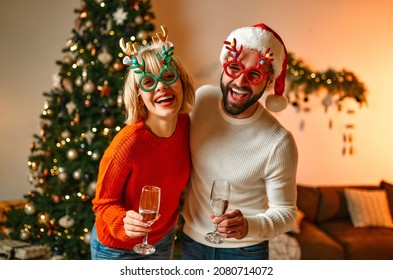 Merry Christmas and Happy New Year! Couple in Santa hats and reindeer antlers in funny horned glasses sitting on the floor near the Christmas tree with glasses of champagne, waiting for the holiday. - Powered by Shutterstock