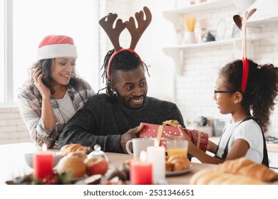 Merry Christmas and Happy New Year! African-american family of three, parents with small preteen girl daughter celebrating winter holidays together at home, giving presents gifts - Powered by Shutterstock