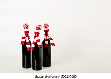 Merry Christmas And Happy New Year. Three Bottles Of Wine In Knitted Caps And Scarfs In Red And White Stripes On A White Background. Selective Focus.