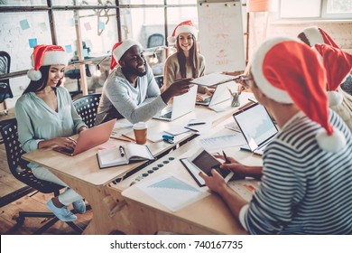 Merry Christmas And Happy New Year 2018!Multiracial Young Creative People Are Celebrating Holiday In Modern Office. Group Of Young Business People Are Sitting In Santa Hats In Last Working Day. 