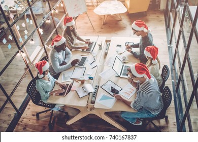 Merry Christmas And Happy New Year 2018!Multiracial Young Creative People Are Celebrating Holiday In Modern Office. Group Of Young Business People Are Sitting In Santa Hats In Last Working Day. 