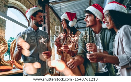 Merry Christmas and Happy New Year 2020!Multiracial young creative people are celebrating holiday in modern office. Group of young business people are drinking champagne with sparkling bengal light.