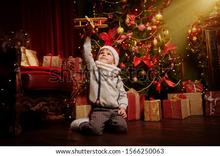 Merry Christmas holidays. Happy little boy plays with airplane at home next to a beautiful Christmas tree. Christmas and New Year concept.