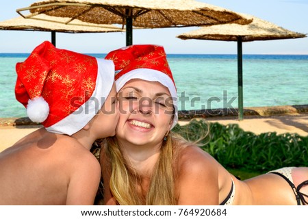  Merry Christmas.Mom and little son are lying on the beach wearing santa hats and celebrating Christmas.