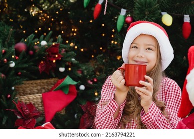 Merry Christmas. Portrait Of Funny Child Girl In Santa Hat Eating Gingerbread Cookies Drinking Hot Chocolate Outside Having Fun. Happy Holidays. Kid Enjoying Holiday. Christmas In July