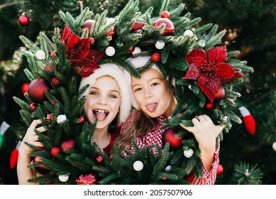 Merry Christmas. Portrait Of Two Happy Funny Children Girls In Santa Hat With Christmas Wreath. Happy Holidays. Fairy Magic. Happy Kids Enjoying Holiday.