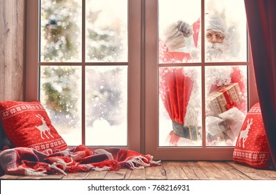 Merry Christmas! Santa Claus Is Knocking At Window. Room Decorated For Holidays. View Indoors Home.