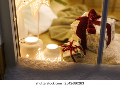 Merry Christmas! Stylish Christmas gifts and glowing lantern in snowy window on background of xmas tree with lights in evening. Atmospheric christmas eve at home. Holiday magical scene - Powered by Shutterstock