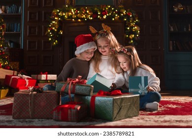 Merry Christmas Xmas holiday. Children unpacking open up gift box near Christmas tree. Kids in living room with Christmas tree fireplace opening gift box with surprise faces. Christmas eve at home - Powered by Shutterstock