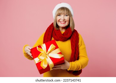 Merry elderly woman 50s years old wear yellow knitted sweater red scarf Santa hat posing hold present box with gift ribbon bow isolated on plain pink background. Happy New Year Christmas 2023 concept - Powered by Shutterstock