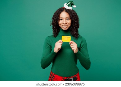 Merry fun little kid teen girl wear hat casual clothes posing hold mock up of credit bank card isolated on plain green background studio portrait. Happy New Year celebration Christmas holiday concept - Shutterstock ID 2396398875
