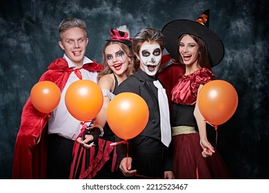 Merry Halloween party. Teenage friends in carnival costumes have fun celebrating Halloween. Skeleton, witch, clown and vampire. Studio portrait on vintage background. - Shutterstock ID 2212523467